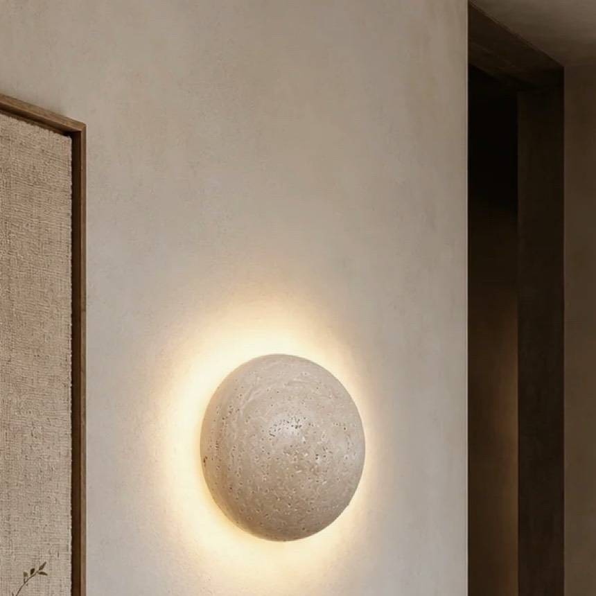 Kasumi wall light, a natural travertine disc casting a soft halo on the wall