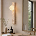 Taki wall light, a slim travertine column with a glass globe beside a bathroom mirror