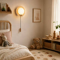 Tsuki wall light, a natural travertine disc with a glass globe in a calm bedroom